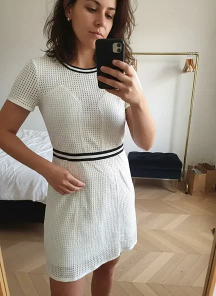 Photo d'une robe blanche portée par un mannequin IA femme souriante dans une chambre