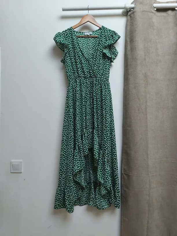 Robe longue verte à motifs sur cintre contre un mur blanc